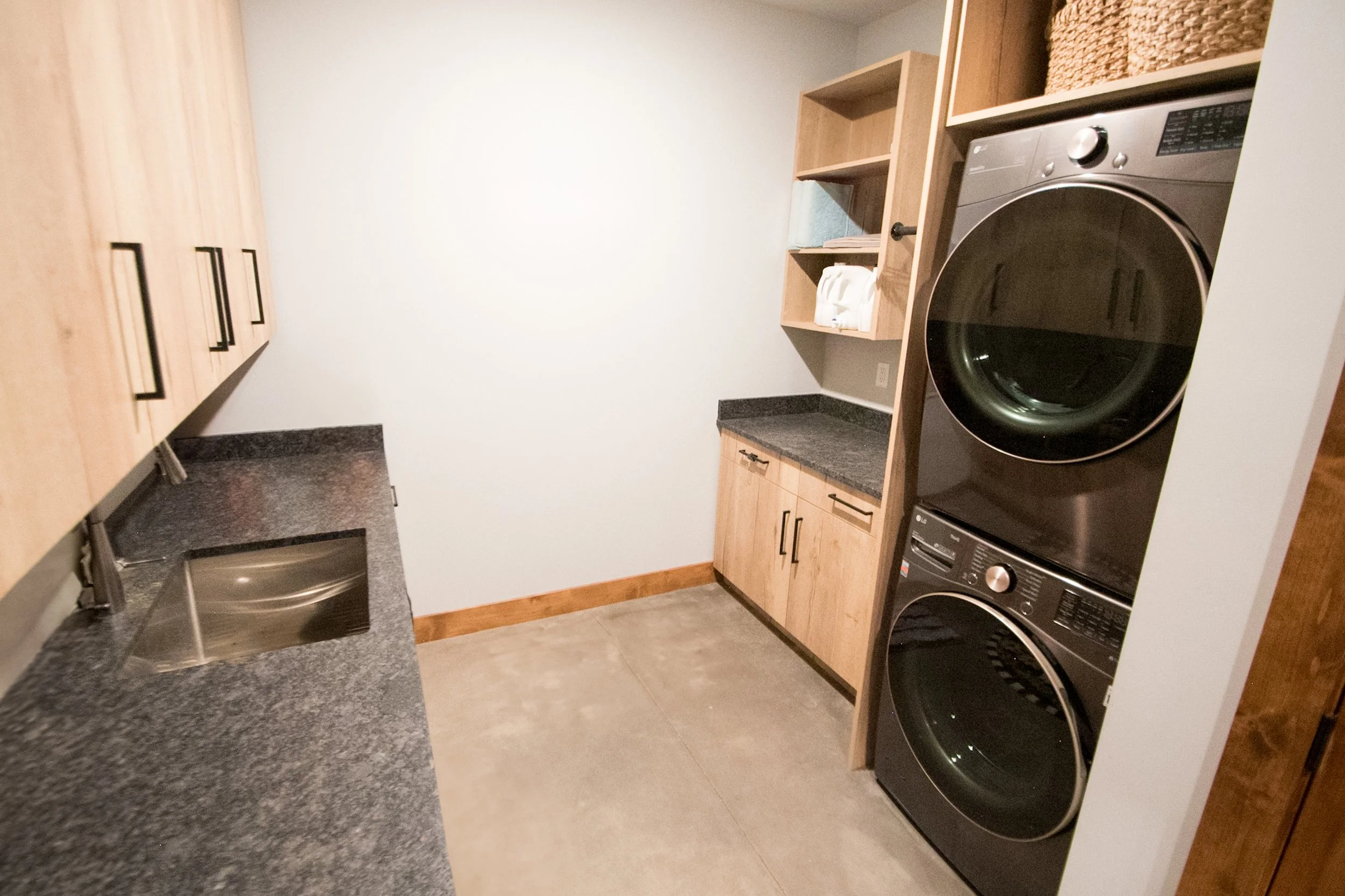 A laundry room with a stacked washer and dryer, wooden cabinets, and black granite countertops.
