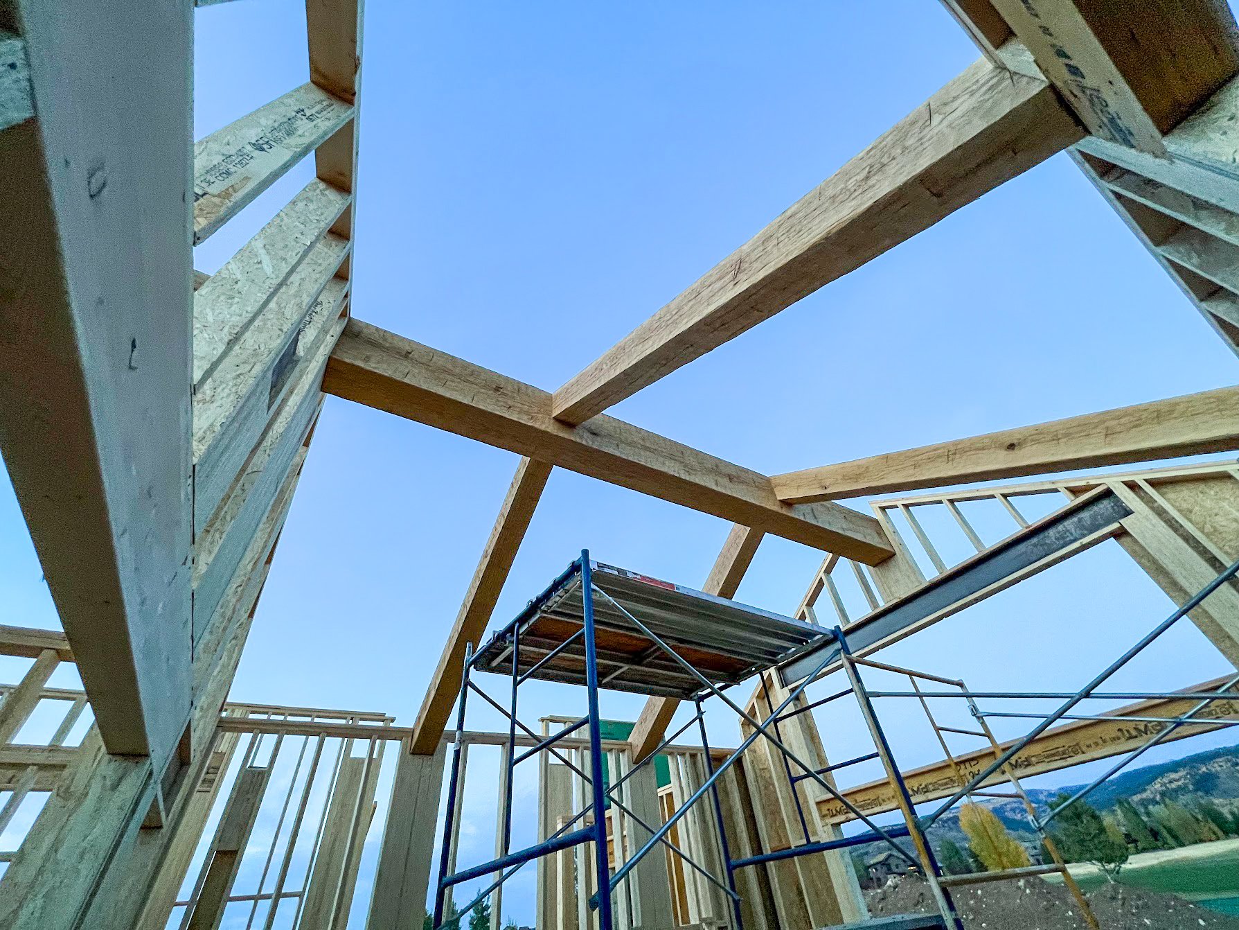 Wooden framing of a building under construction with visible beams and scaffolding against a clear blue sky.