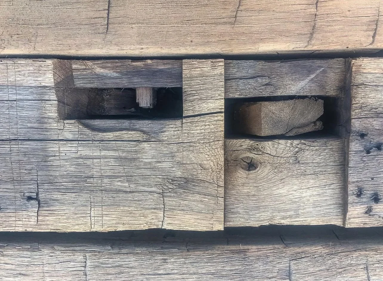 Close-up of weathered wooden surface with two rectangular cutouts, one containing a small wooden peg and the other holding a piece of wood.