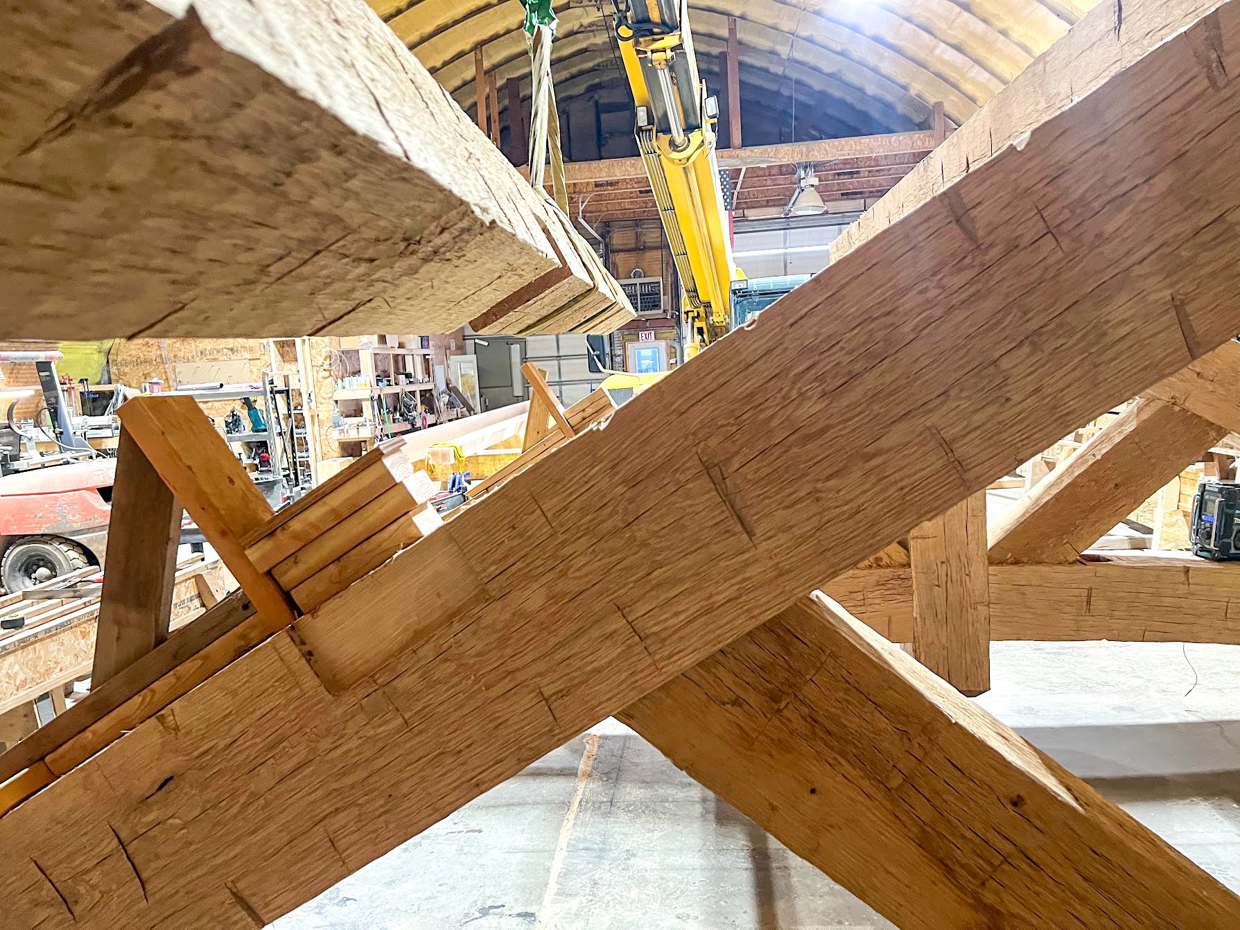 Close-up view of a wooden roof framework under construction in a workshop with tools and equipment in the background.