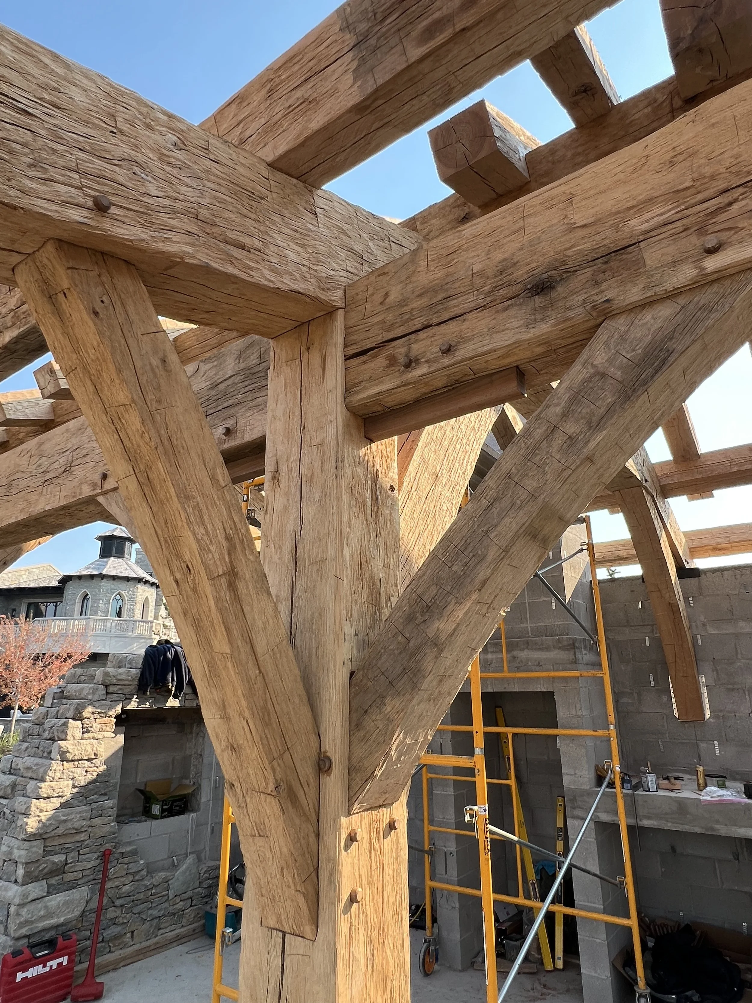 Close-up of wooden beams and support structure under construction, with scaffolding and construction tools in the background.