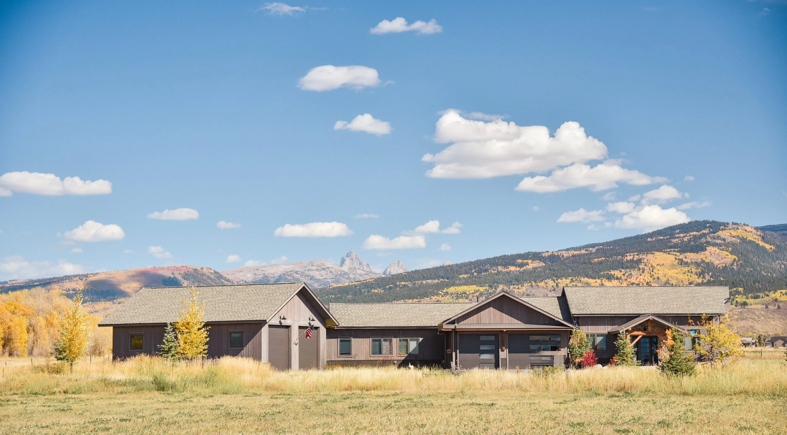 A modern house with a mountainous landscape in the background under a partly cloudy blue sky.