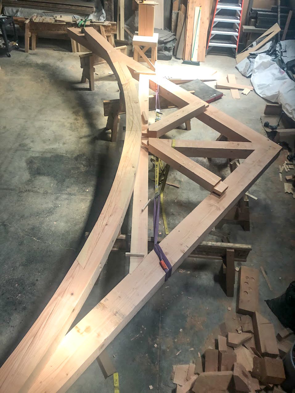 Wooden structure being built on workbenches in a workshop, with tools and wood scraps around.