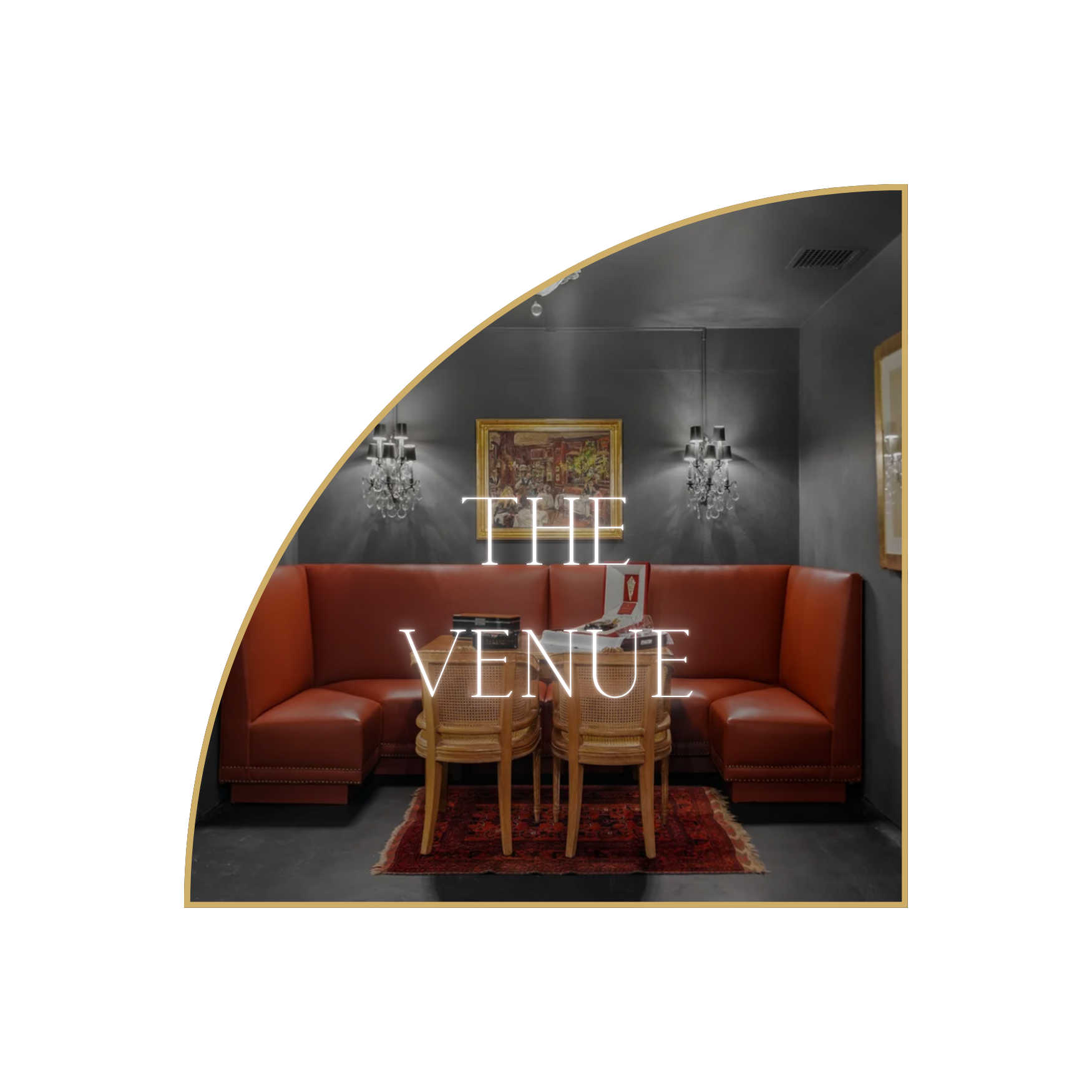 Interior of a dimly lit lounge with gray walls, chandelier wall sconces, framed artwork, a red leather upholstered corner bench, and wooden chairs around a small table. Neon sign reading 'THE VENUE' is displayed on the wall.