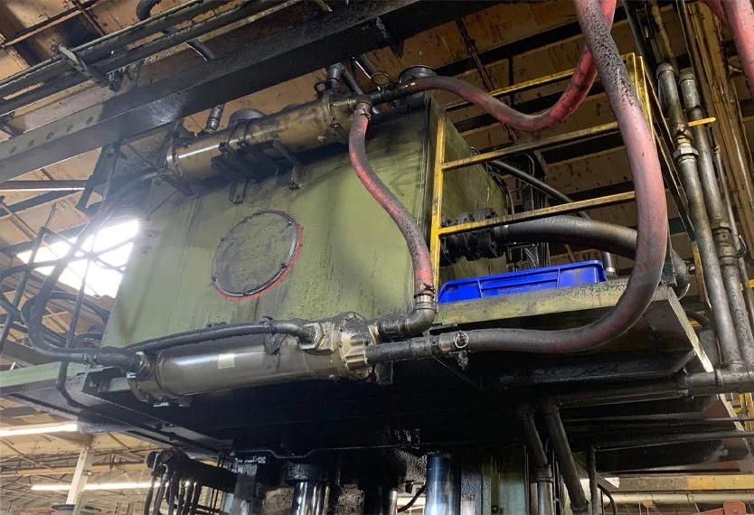 Industrial machinery with pipes, a green tank, and a blue container mounted on a metal platform in a factory.
