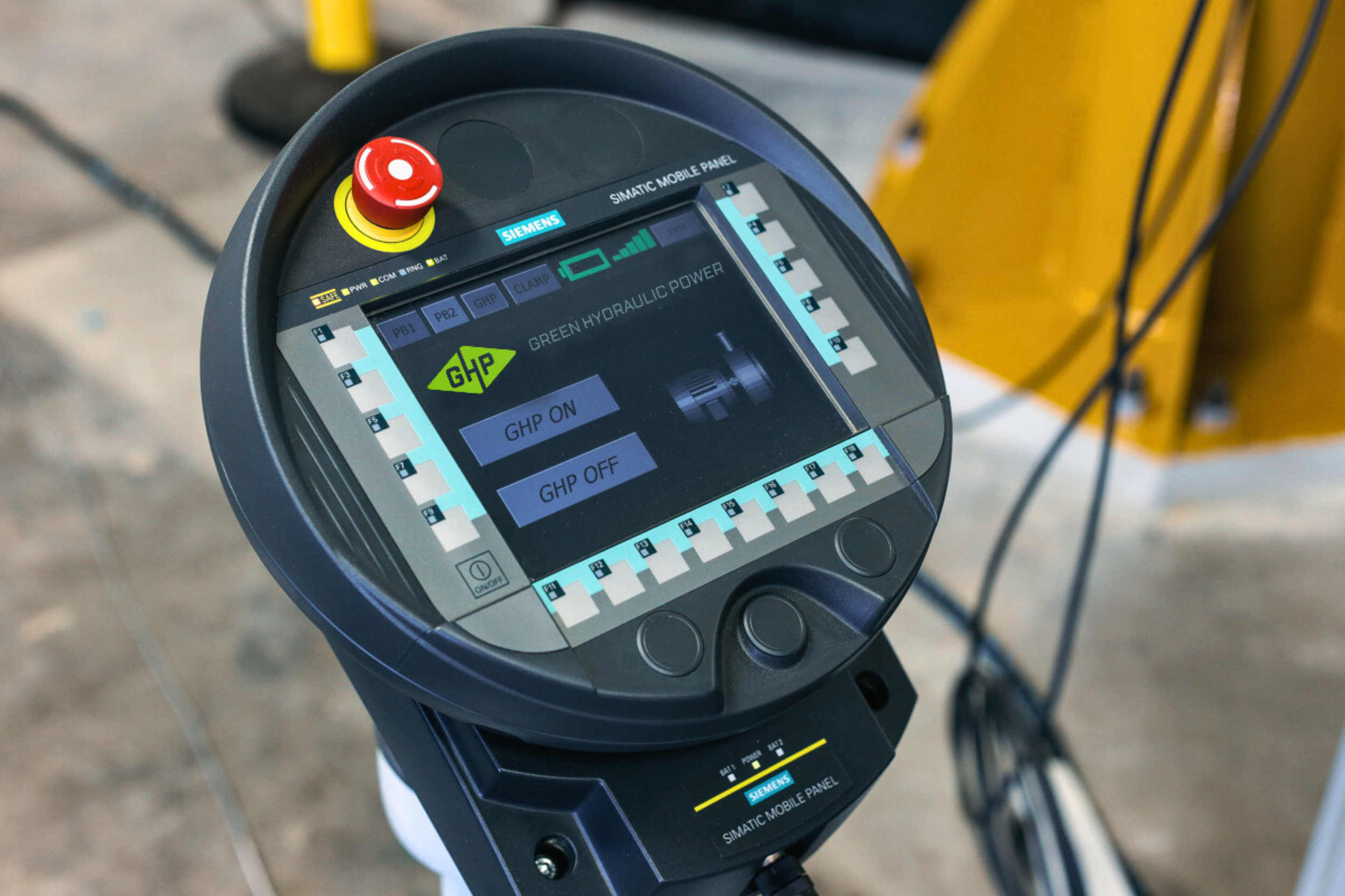 Close-up of a Siemens hydraulic control panel with a touchscreen display showing options to turn GHP on or off, with a yellow emergency stop button on top and connected cables in the background.