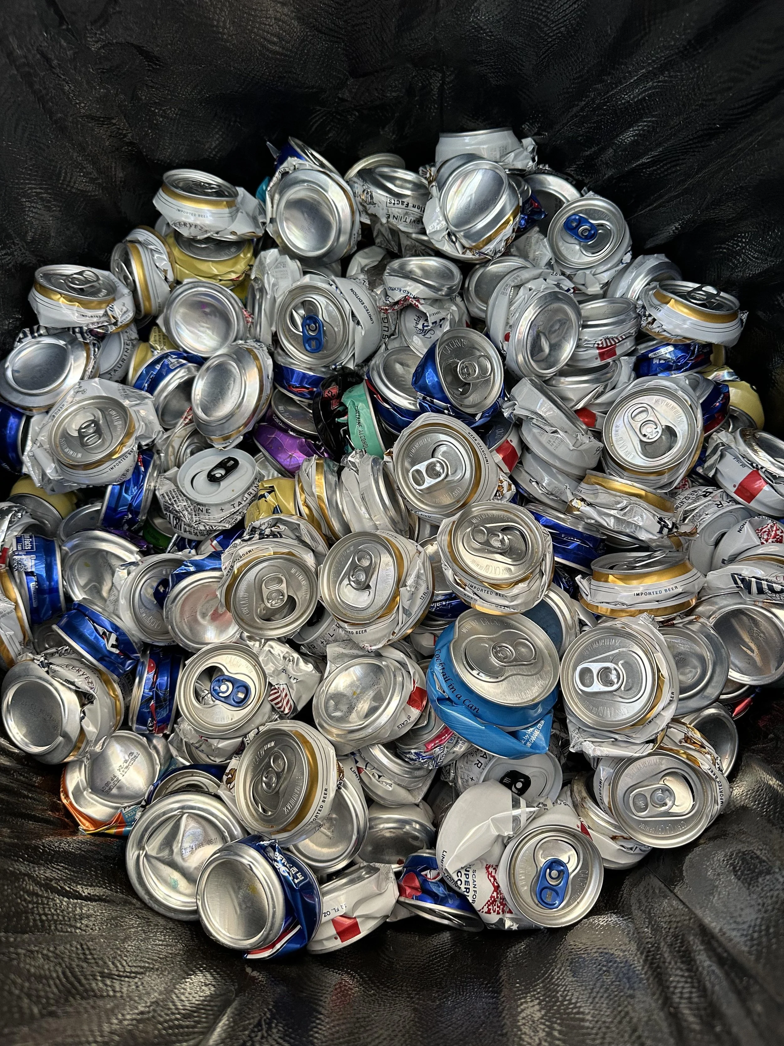 A trash bin filled with crushed aluminum beverage cans.