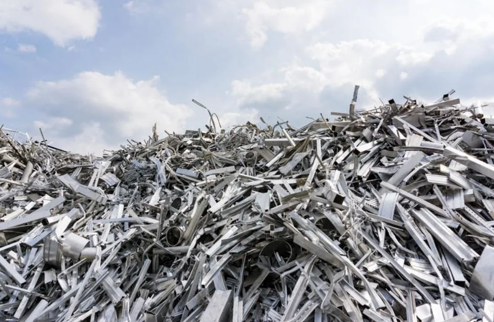 A large pile of aluminum scraps and metal debris outdoors under a cloudy sky.