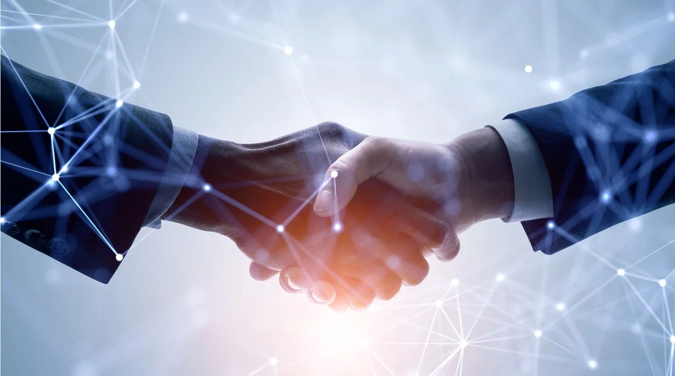 Two people in business suits shaking hands, with a digital network overlay in the background.
