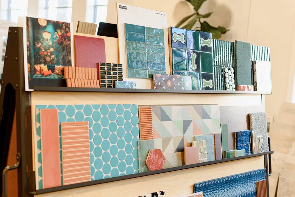 Display of colorful ceramic tiles arranged on a tiered stand, featuring various patterns and textures in shades of blue, pink, green, and orange.