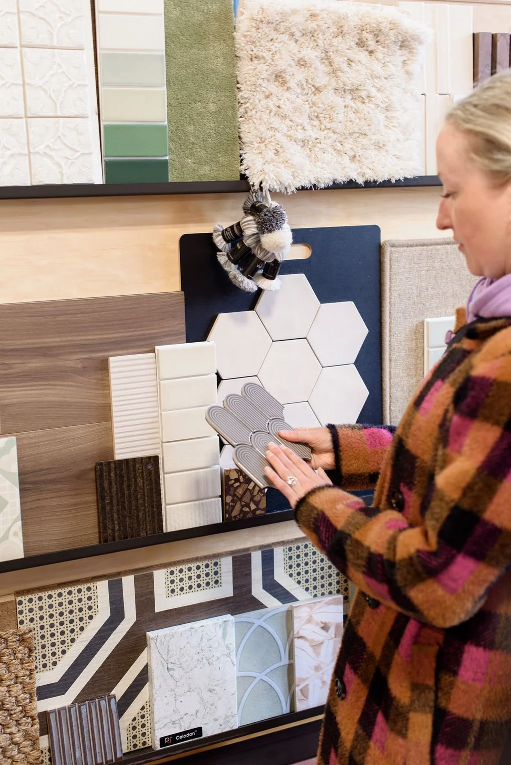 Woman wearing a checkered coat browsing tile and flooring samples in a showroom.