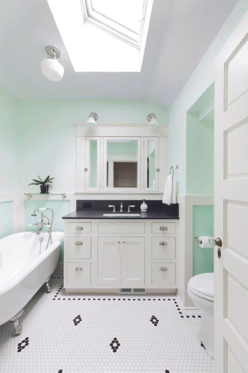 Bright bathroom with white clawfoot tub, black countertop vanity, mint green walls, and a skylight ceiling light.