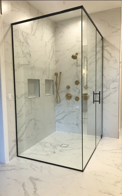Modern glass shower with marble walls and gold fixtures, including a showerhead and controls, in a contemporary bathroom.