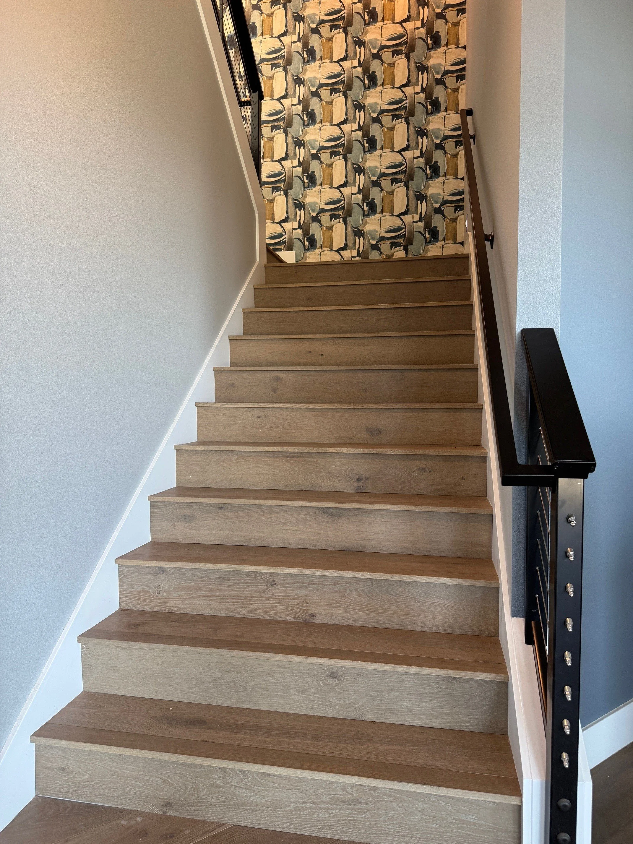 Wooden staircase with a black metal and wood handrail, wall with abstract patterned wallpaper at the top of the stairs.