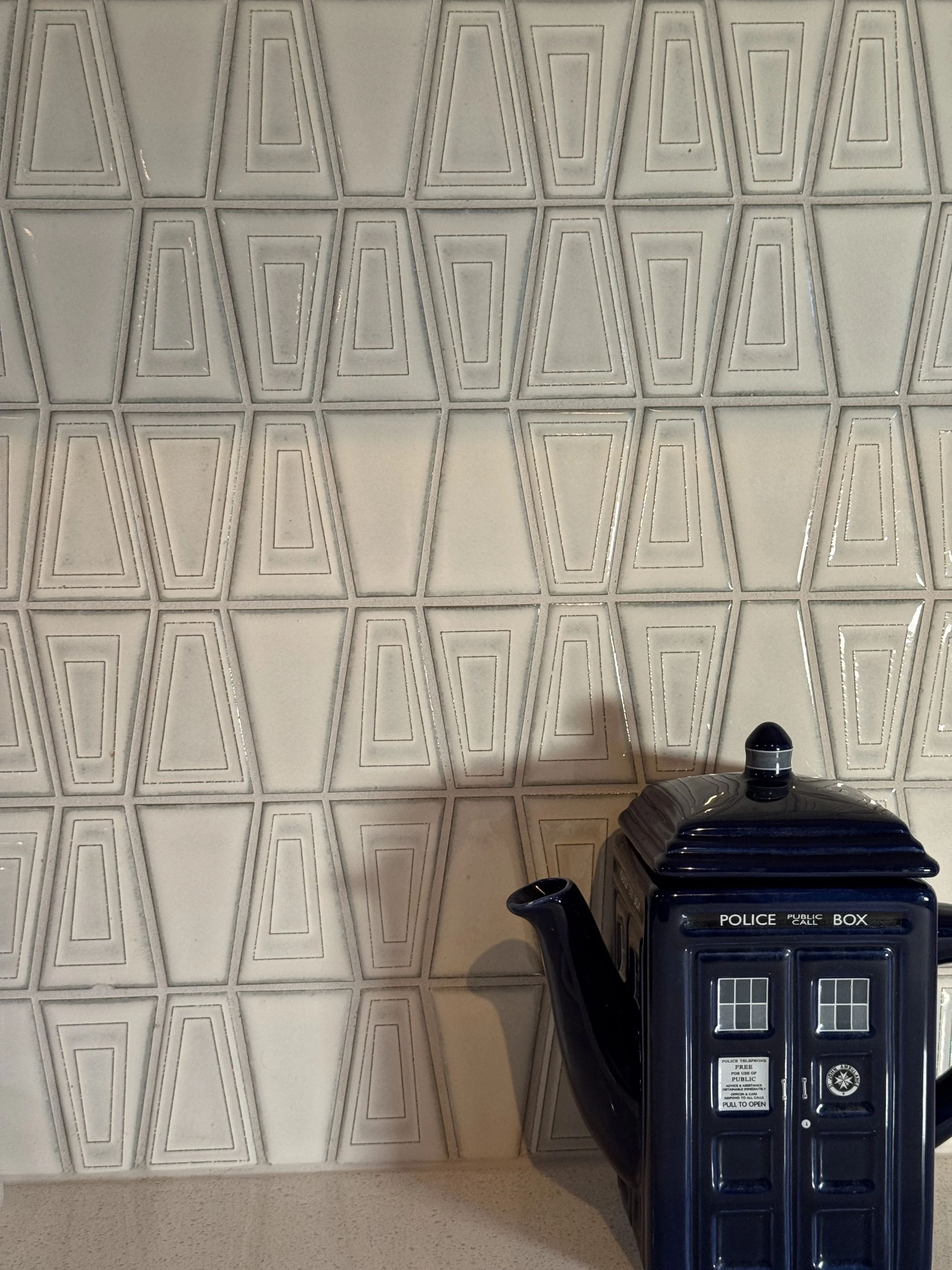 Teapot shaped like a police box on a beige countertop in front of a geometric patterned wall.