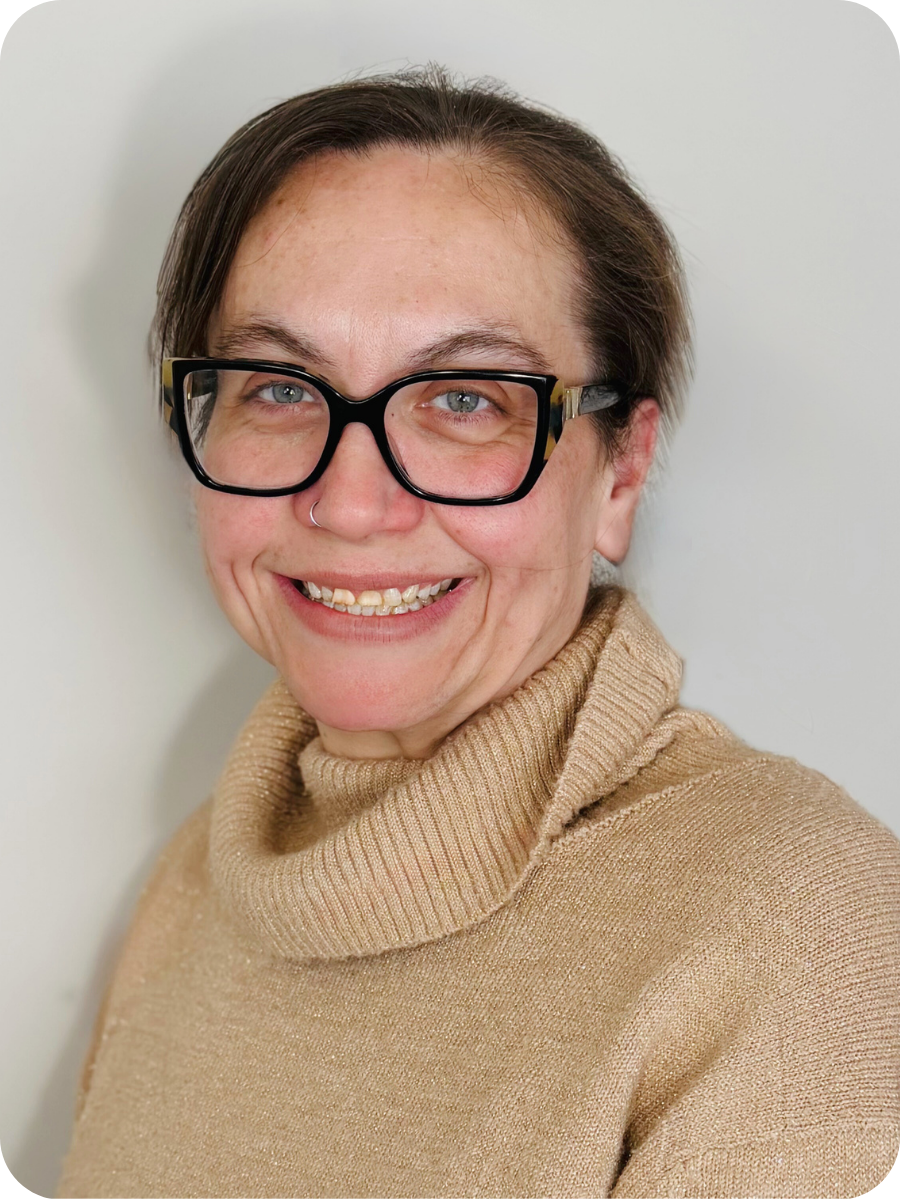 A headshot of a woman in a beige sweater and glasses in front of a white backdrop