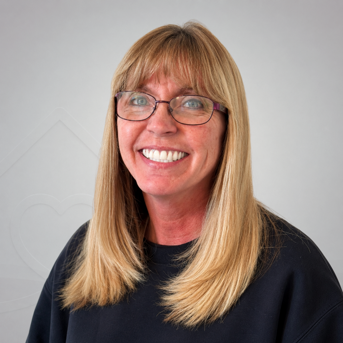 Smiling woman with long blonde hair, glasses, and a black top against a plain light-colored background.