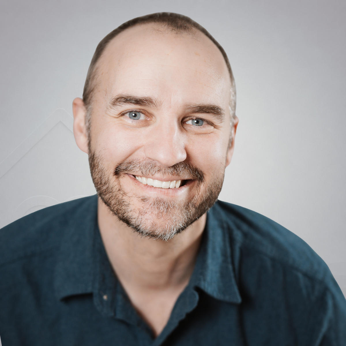 Smiling man with short hair, beard, and mustache wearing a dark blue shirt against a gray background.