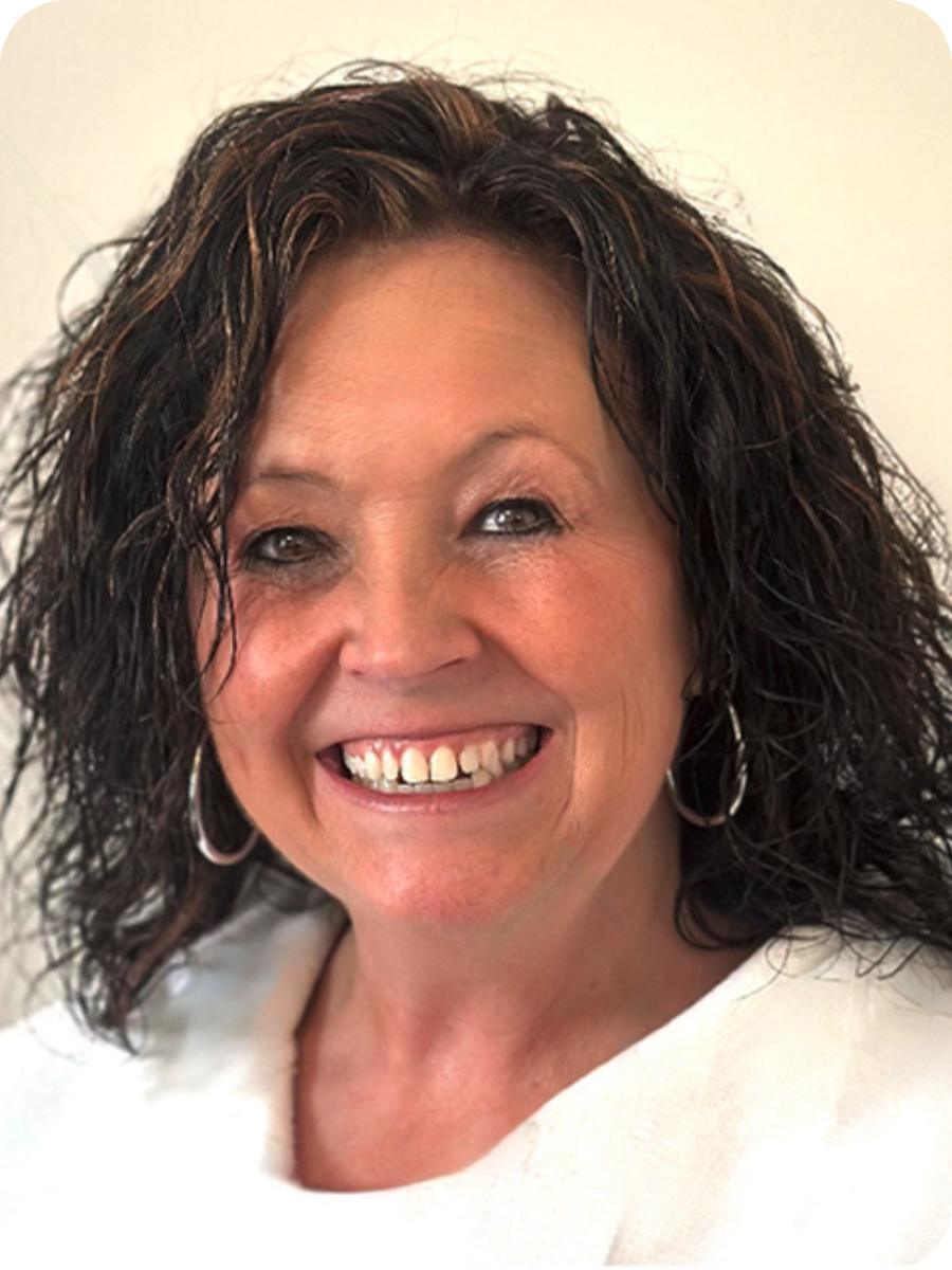 Smiling woman with curly dark hair, hoop earrings, and a light-colored top against a plain background.