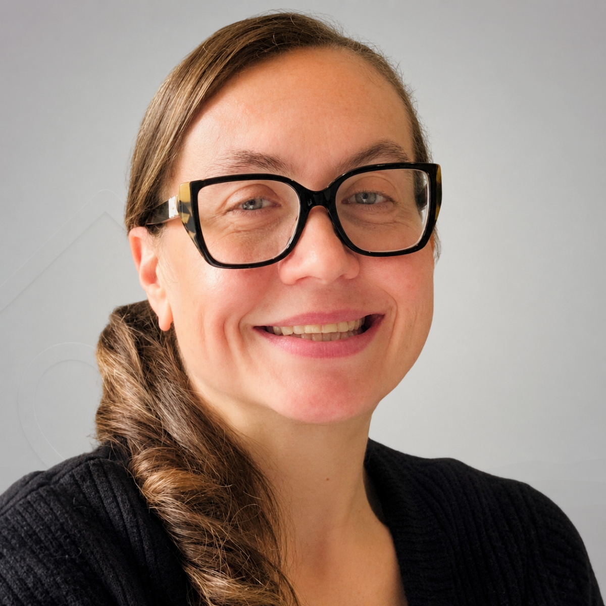 A headshot of a woman in a beige sweater and glasses in front of a white backdrop