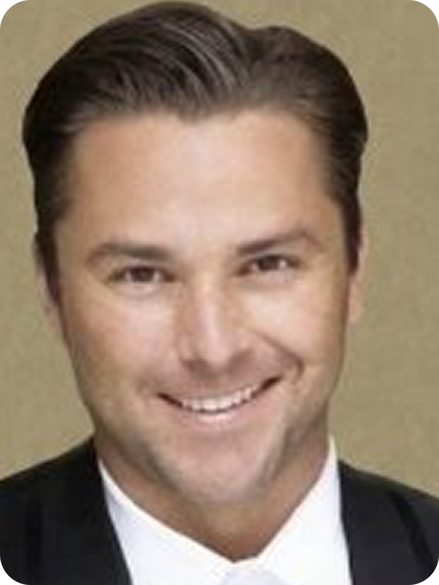 Portrait of a man with slicked-back dark hair, wearing a black tuxedo with a white shirt.