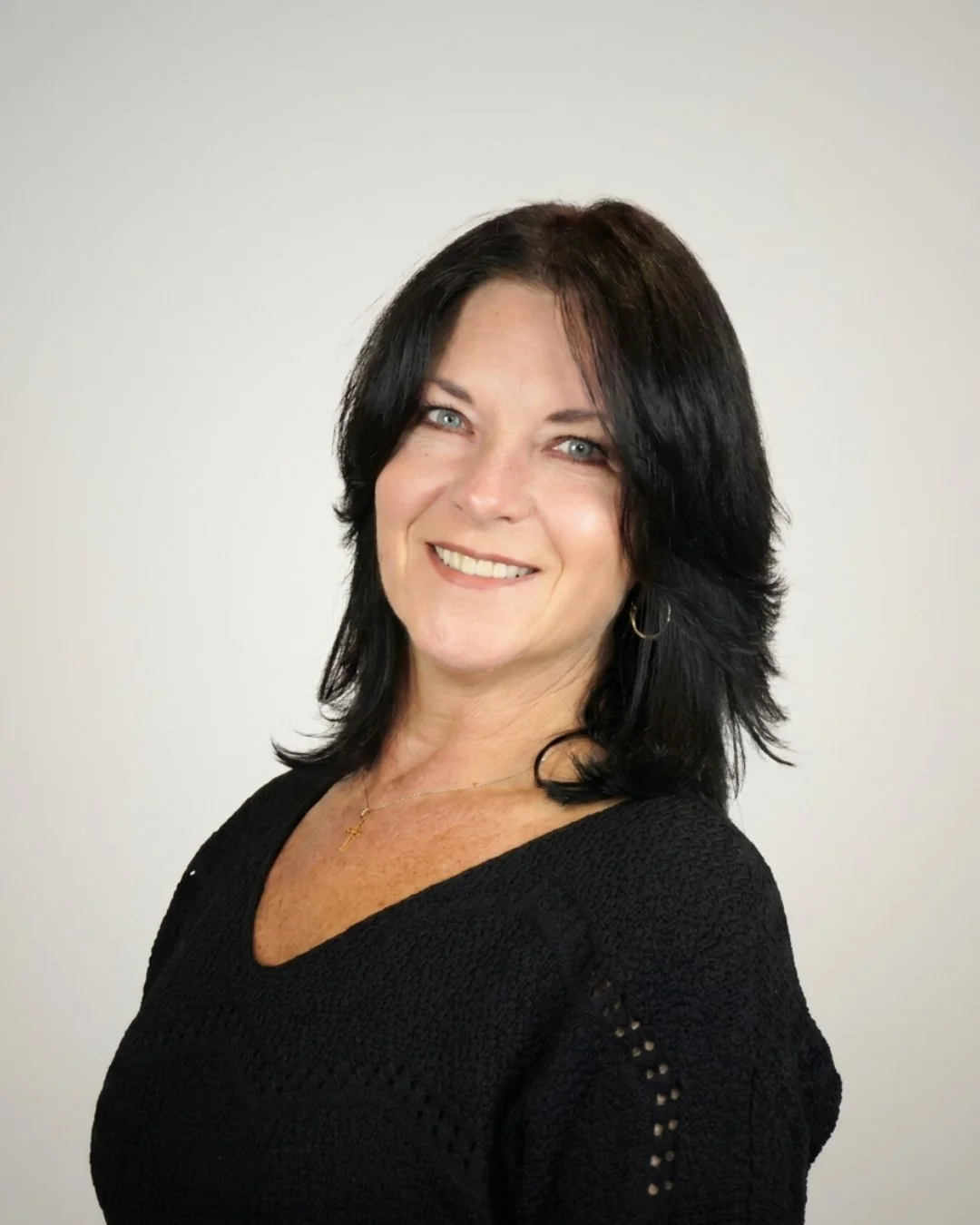 A woman with black hair, blue eyes, and wearing a black shirt, looking at the camera against a plain neutral background.