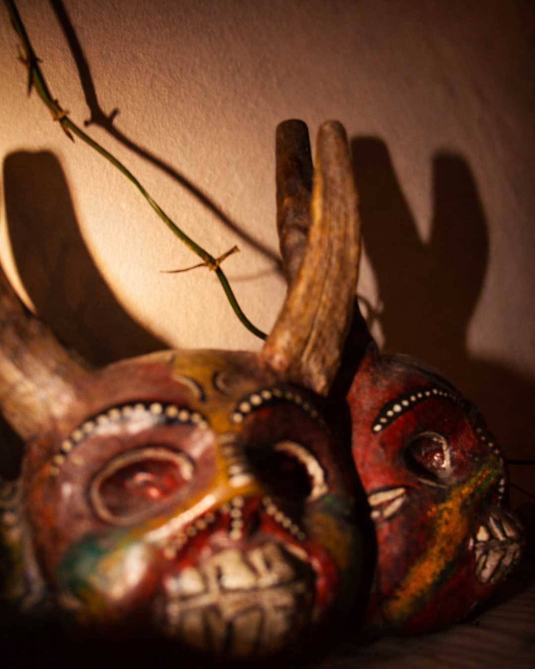 Máscaras tradicionales mexicanas de colores, con detalles en blanco y negro, colocadas en una superficie, con sombra proyectada en la pared.
