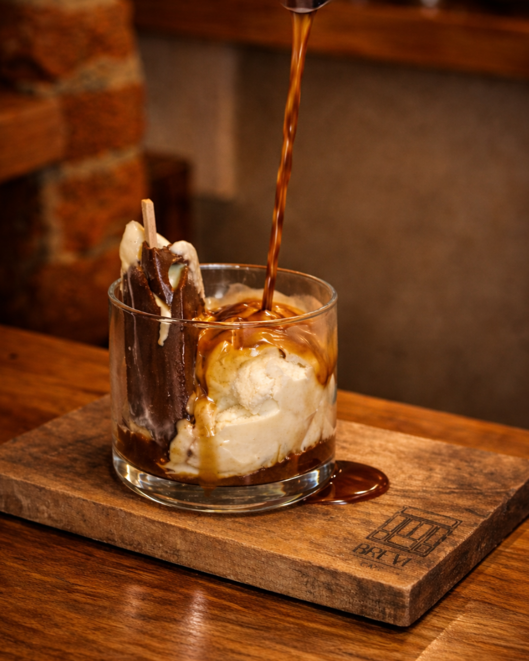 Helado de vainilla con chocolate y caramelo en un vaso de cristal, con jarra de chocolate siendo vertido.