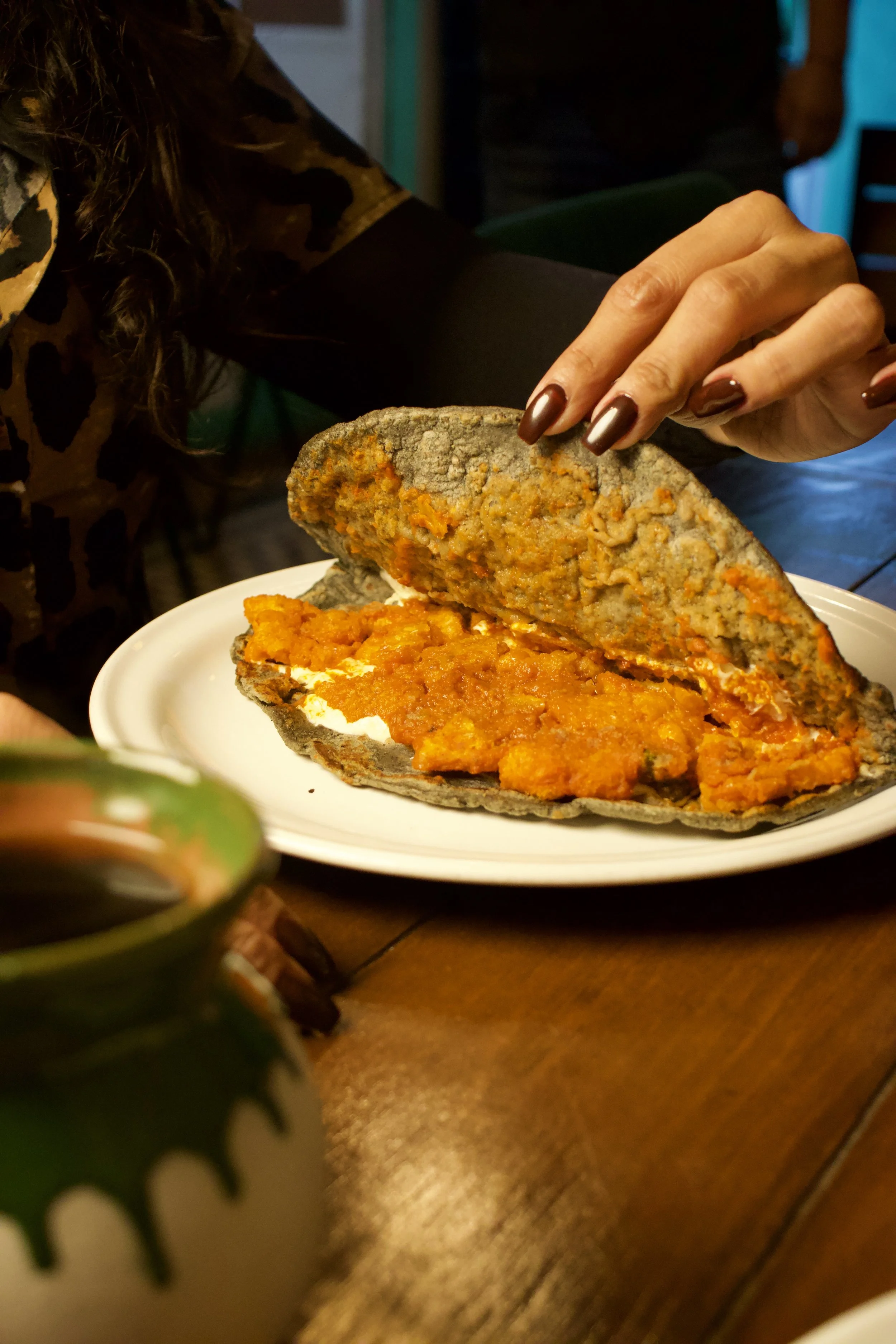 Persona sirviendo un platillo con huevo y salsa en un plato ovalado, en un ambiente de restaurante o cafetería.