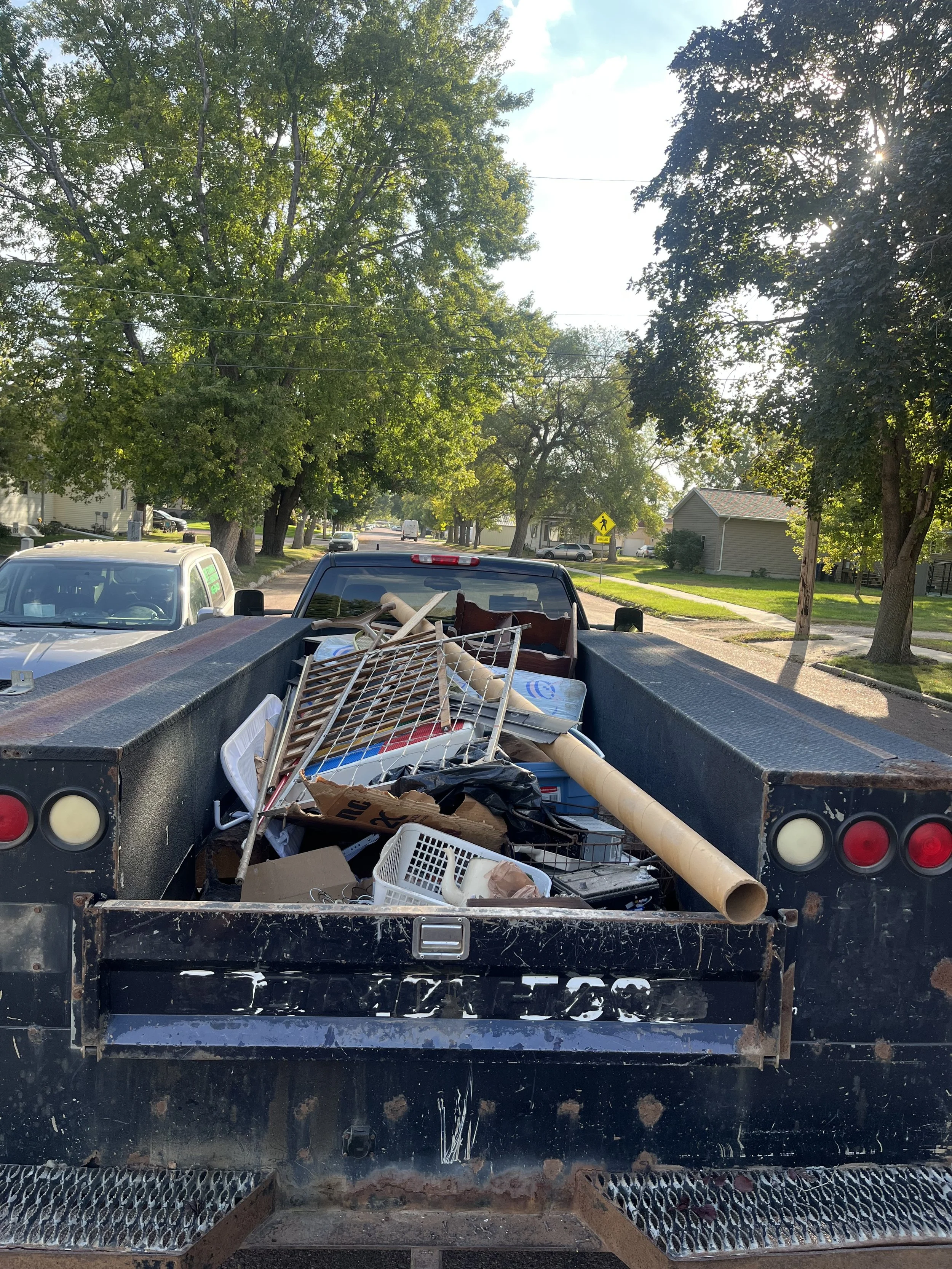 Pickup truck carrying construction debris and household items on a suburban street with trees and houses.