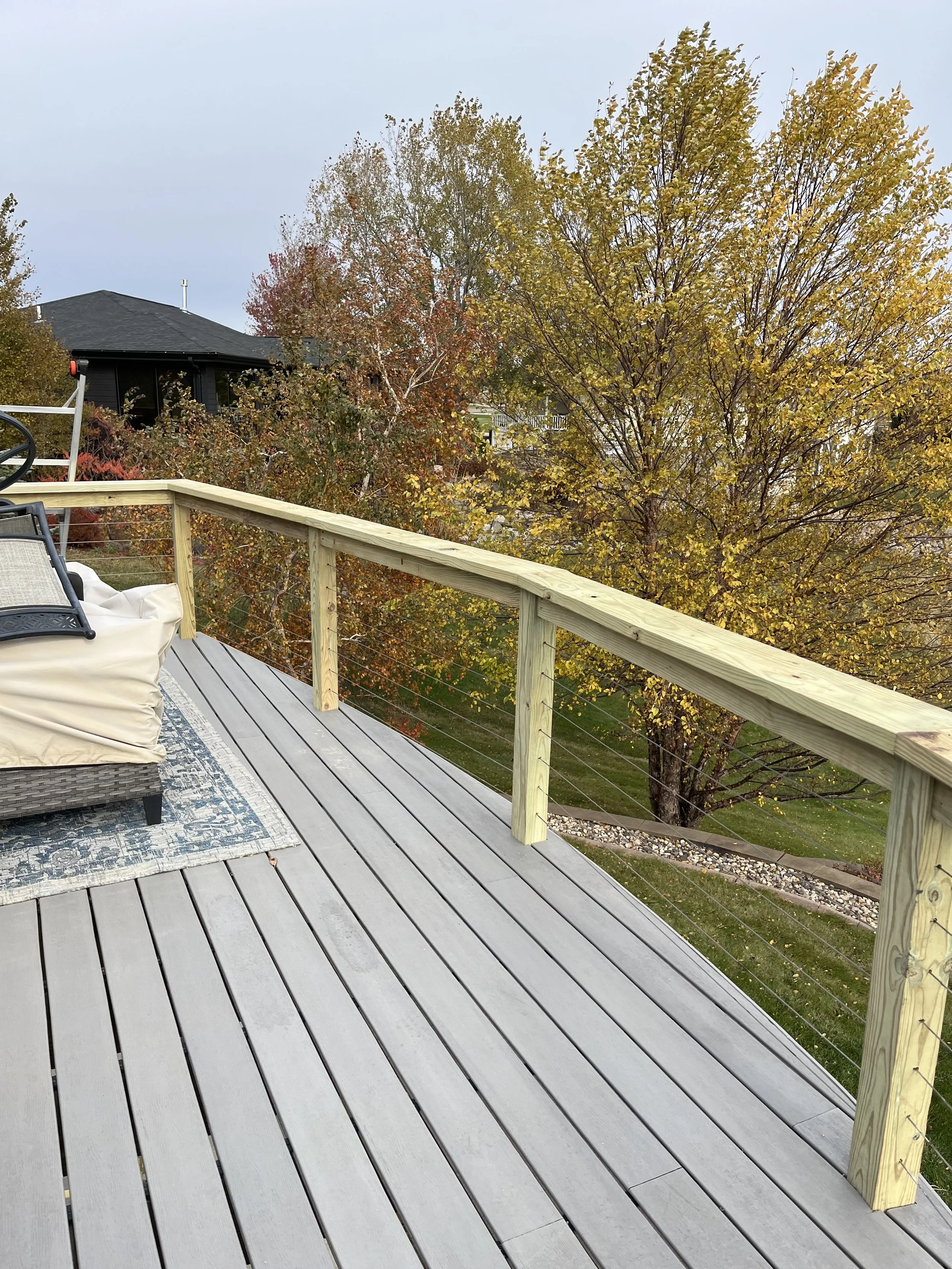 A rooftop deck with wooden railings overlooking a yard with trees showing fall foliage.