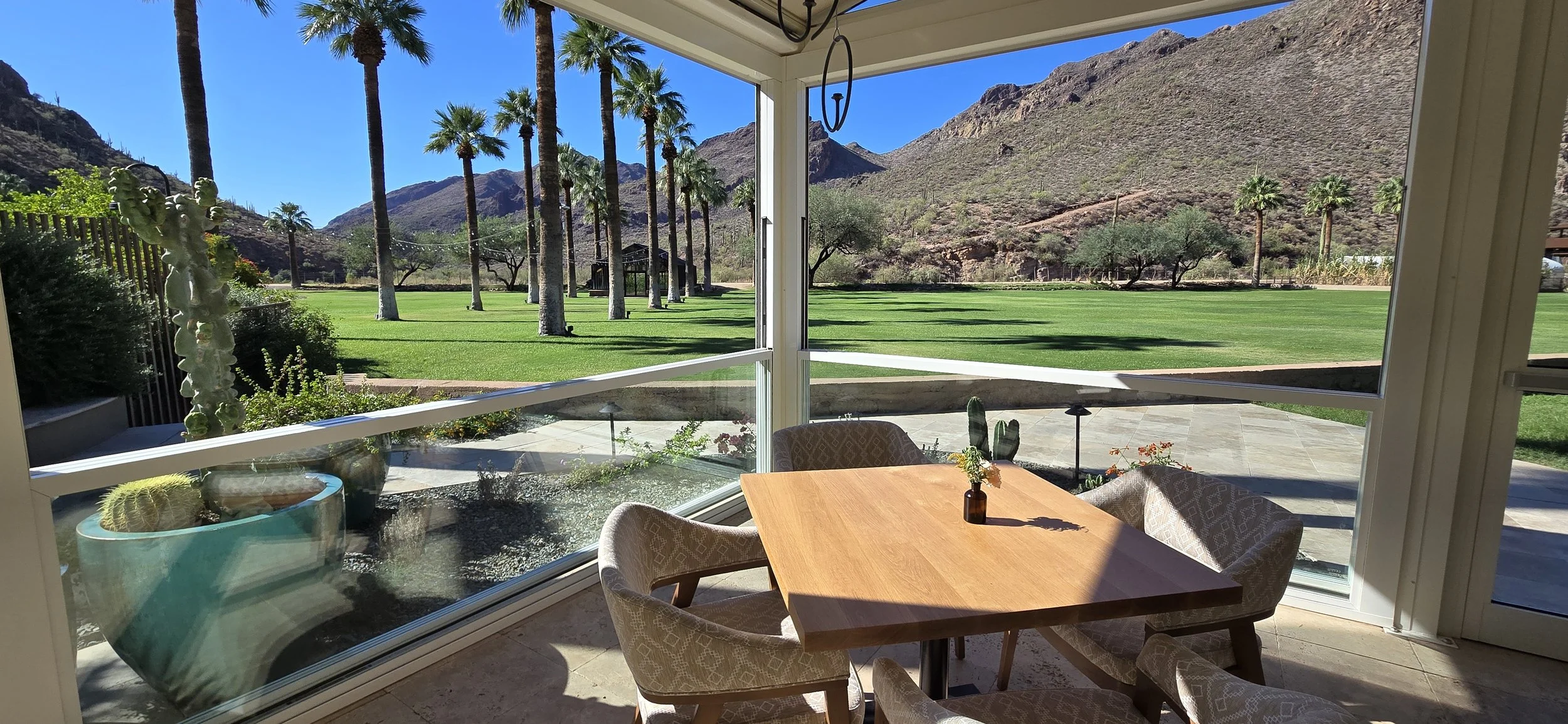 Resort patio enclosure with sliding glass walls and retractable roof, overlooking palm trees.