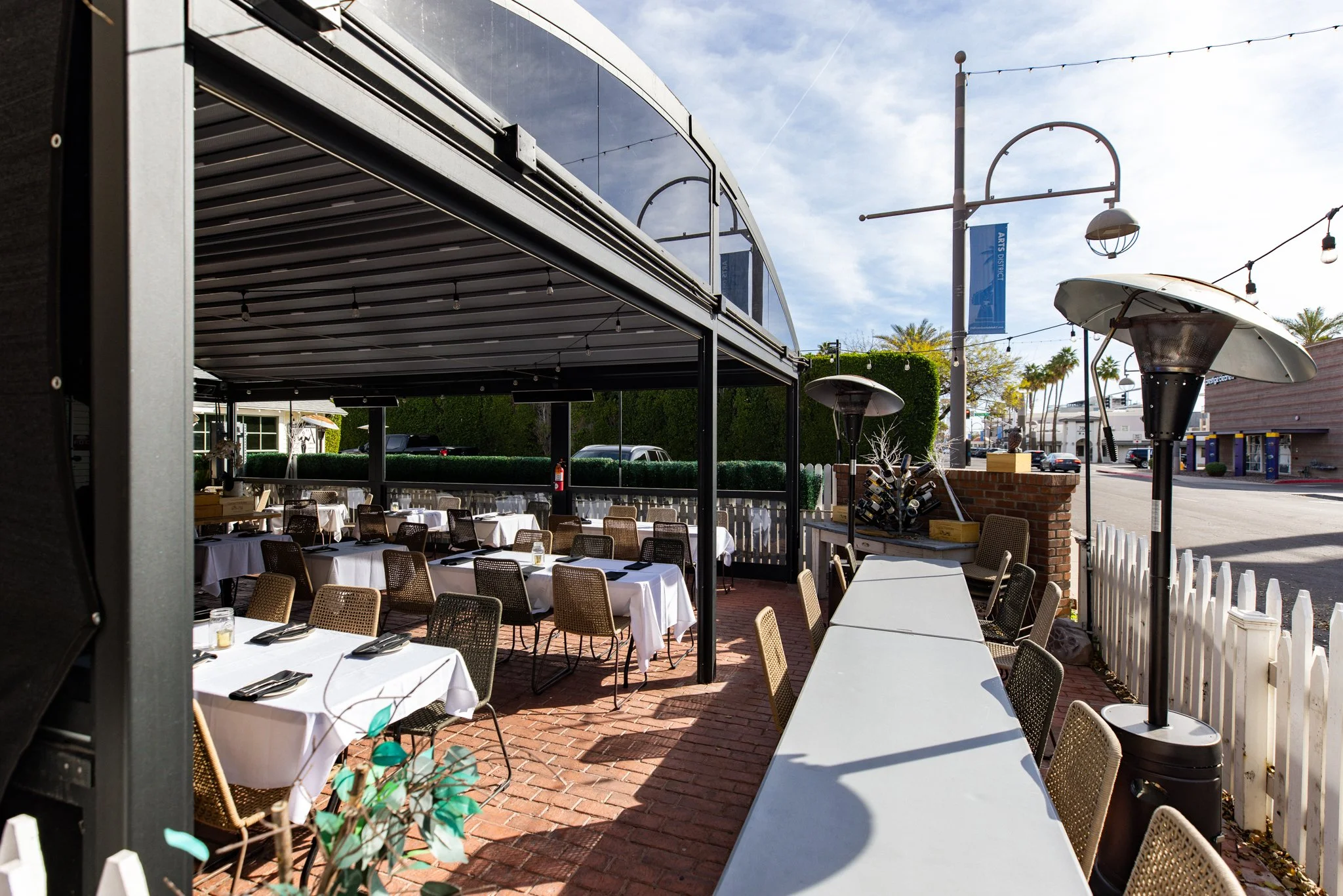 Street-front patio at House Brasserie with the retractable roof closed, picket fence, outdoor heaters, and lunch service setup.