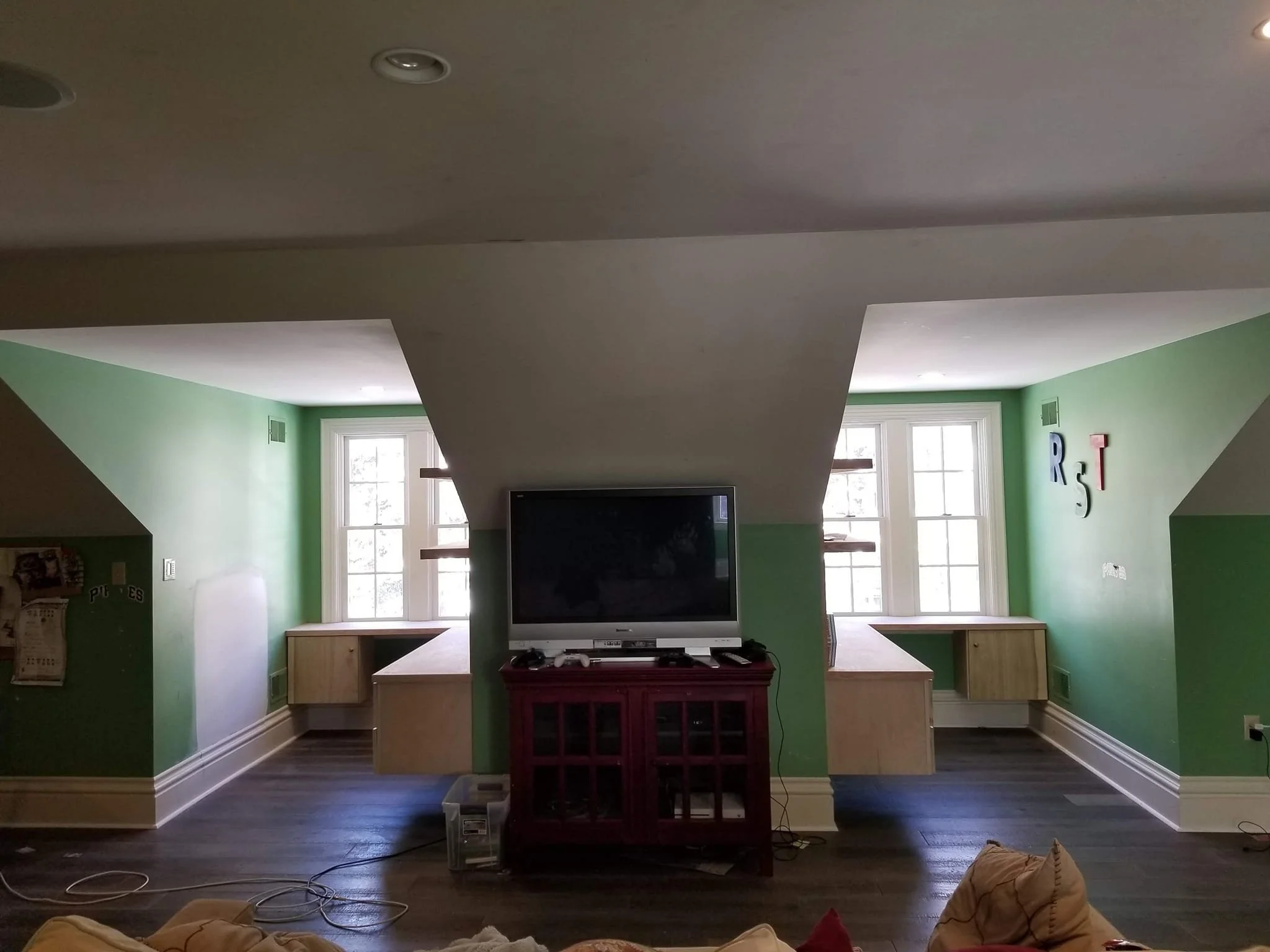 Living room with two green walls, three large windows, a central TV on a red stand, and a seating area with beige cushions.