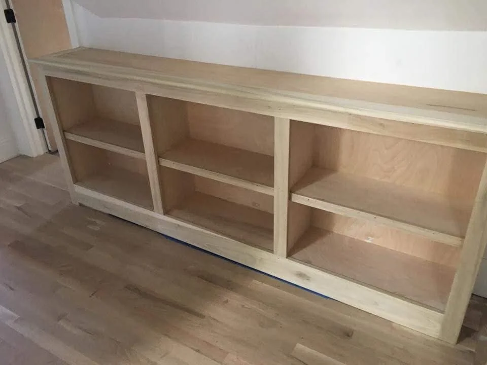 Empty wooden bookshelf with three sections on a hardwood floor.