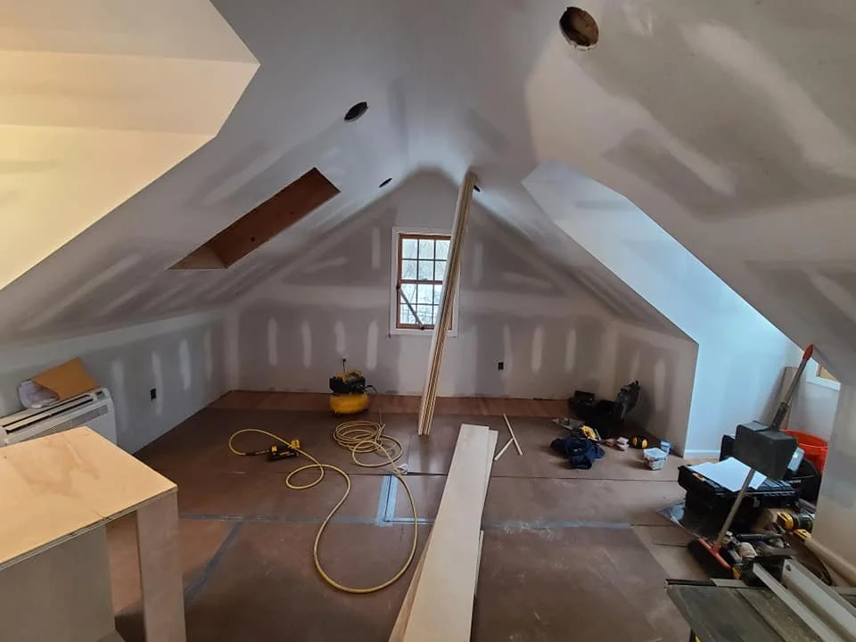 Attic space under renovation with drywall installation, construction tools, and supplies scattered around.