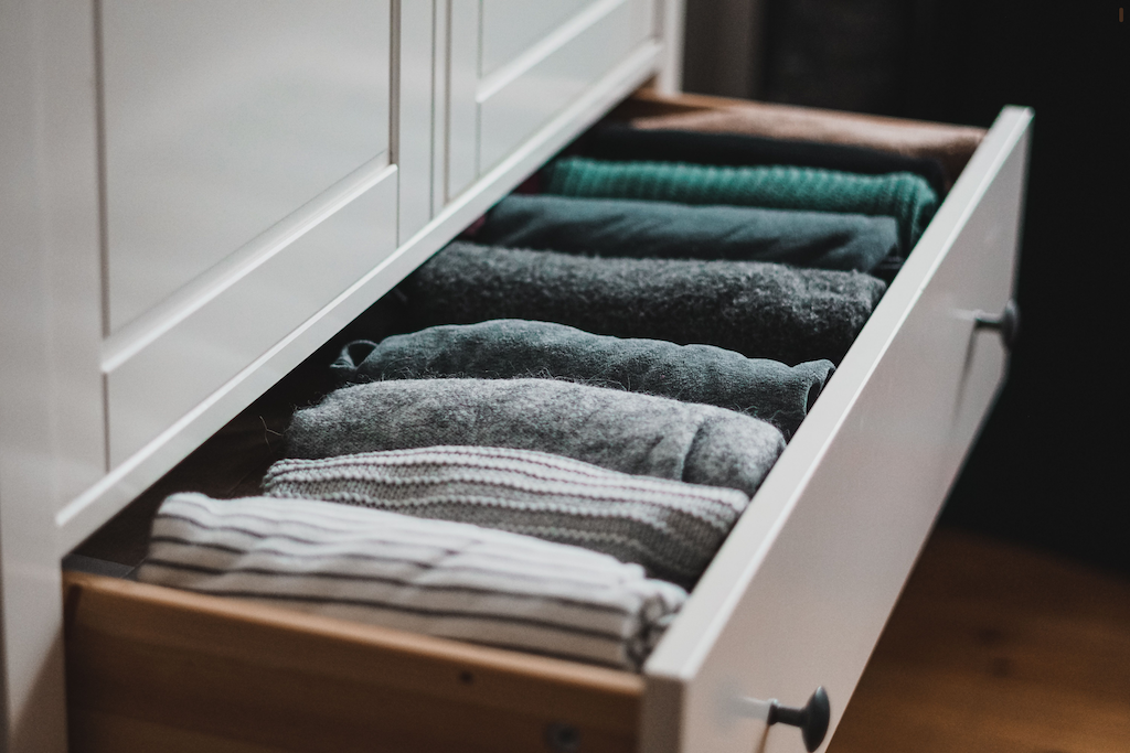 Drawer with neatly folded clothes including striped, gray, black, and green garments.