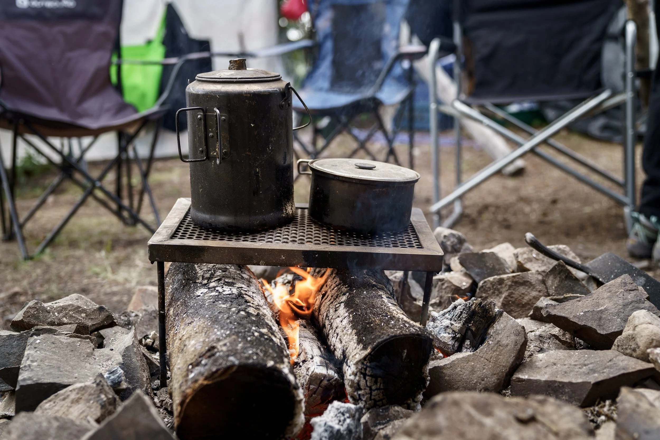 Photo by Anna Crawford. Two pots sit on a metal grate atop an open campfire.
