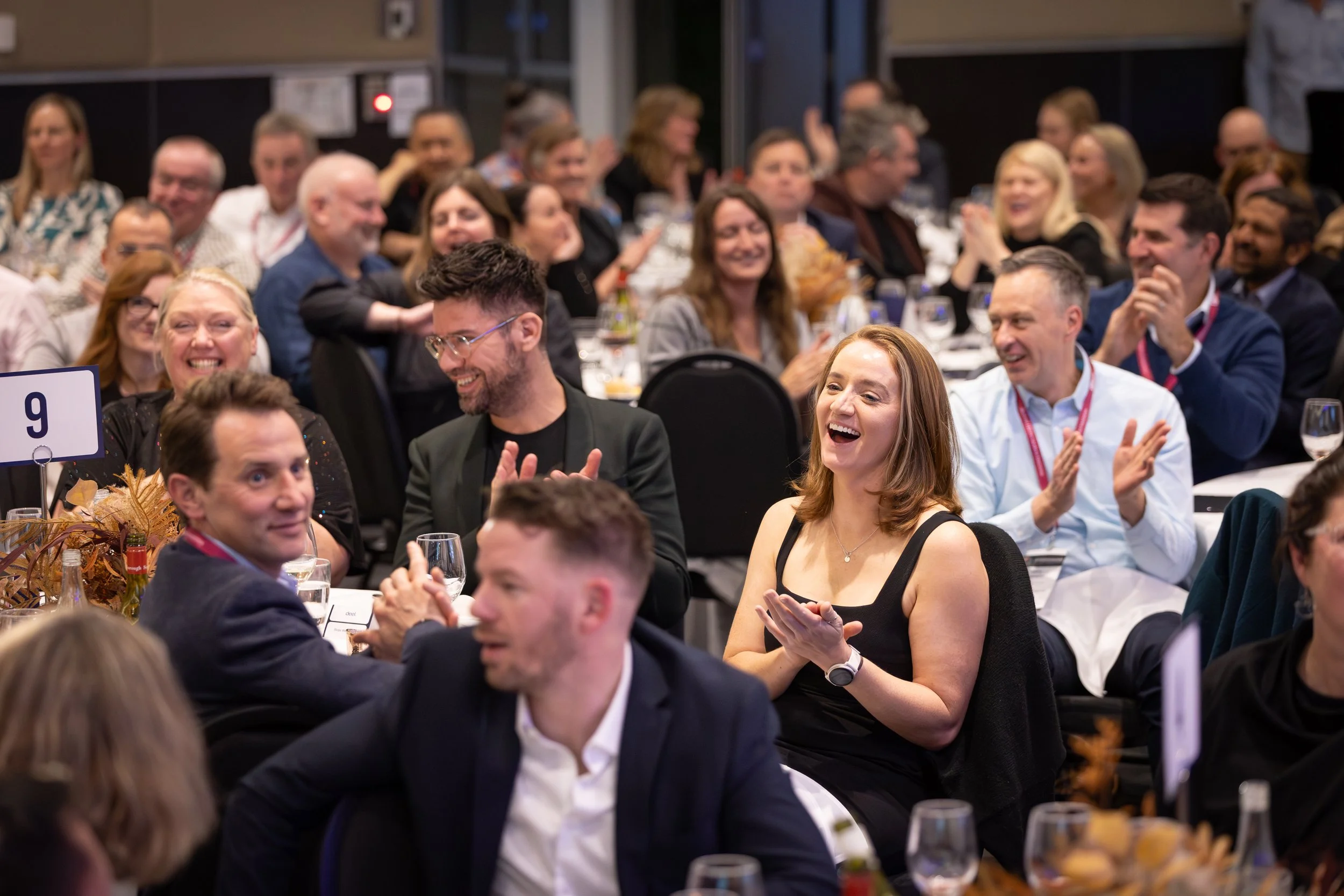 A group of people at a formal event, sitting at tables, laughing and clapping.