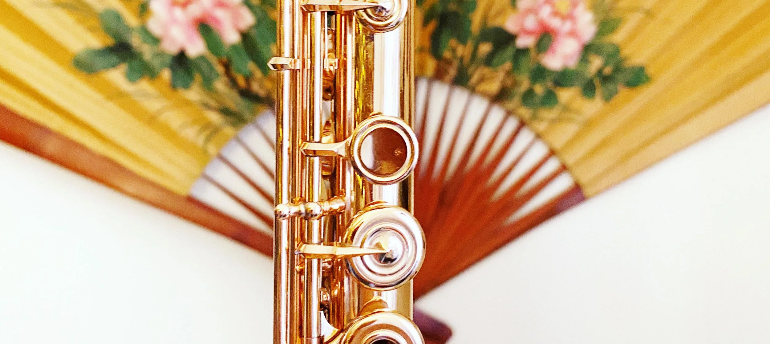 Close-up of a shiny rose gold flute against a background of a decorative folding fan with pink flowers and green leaves.