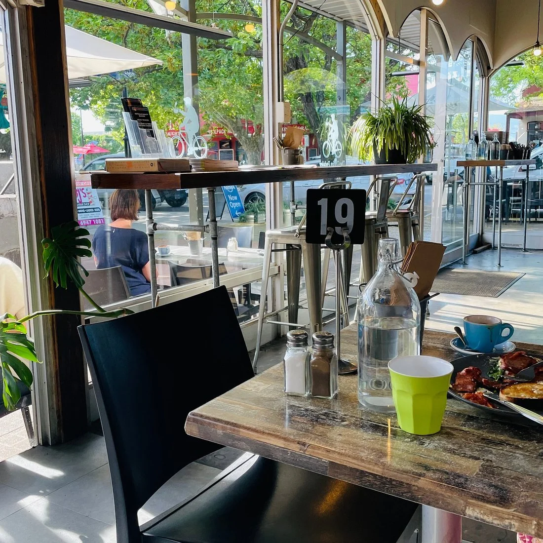 A panoramic view of a valley with lush green fields, scattered trees, and the town of Tumut in the distance, surrounded by rolling hills and mountains under a partly cloudy sky.