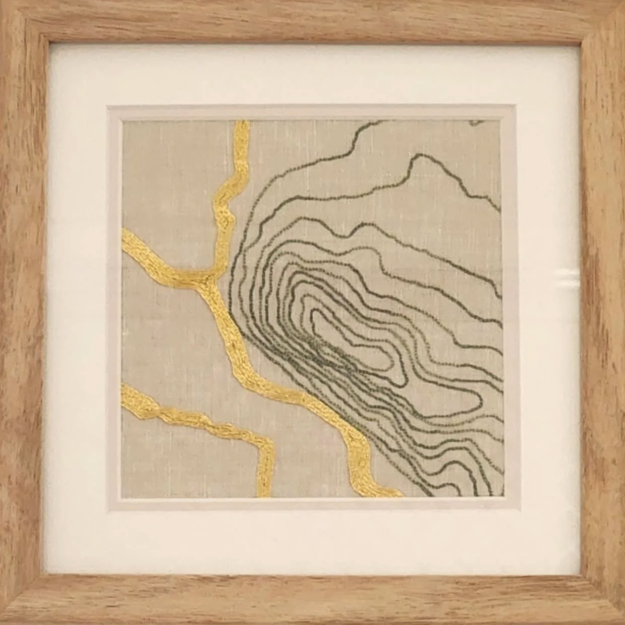 Embroidery artwork of a topographic map with black contour lines and yellow highlighted rivers, framed in wood.
