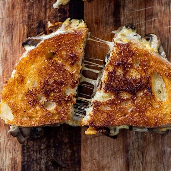Close-up of a cheese toast cut in half, showing melted cheese inside, on a wooden surface.