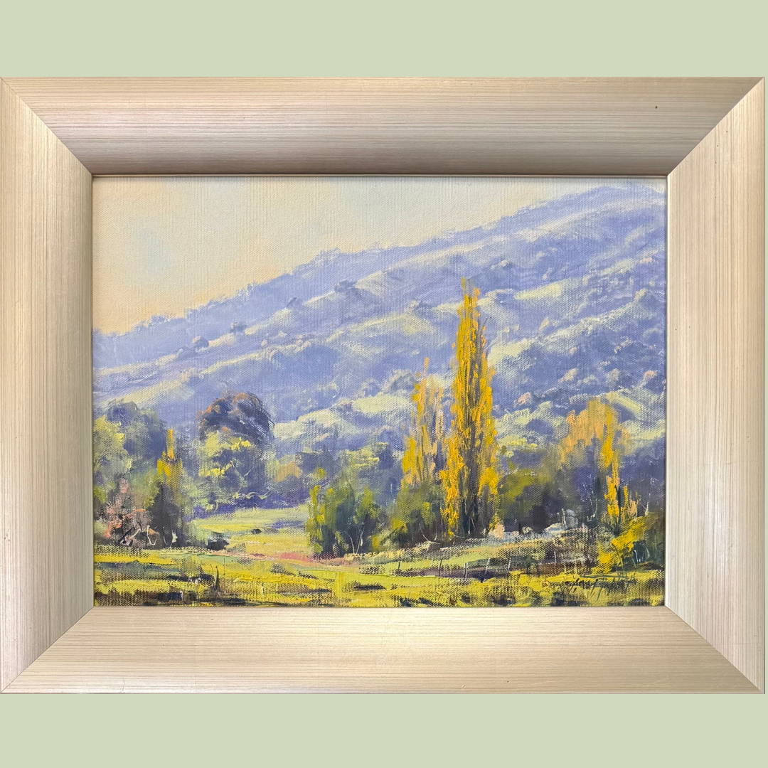 A landscape painting of rolling hills, green fields, and tall yellow trees in the foreground with a distant mountain range in shades of blue in the background.