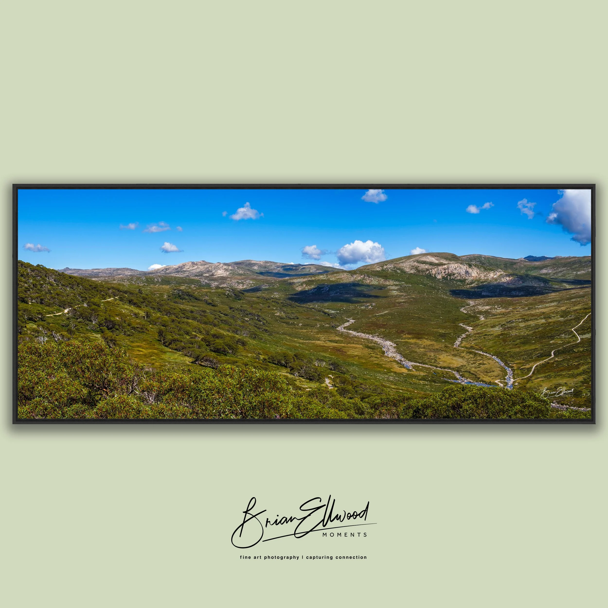 Three landscape photographs hanging on a green wall above a white table with ceramic vases and bowls.
