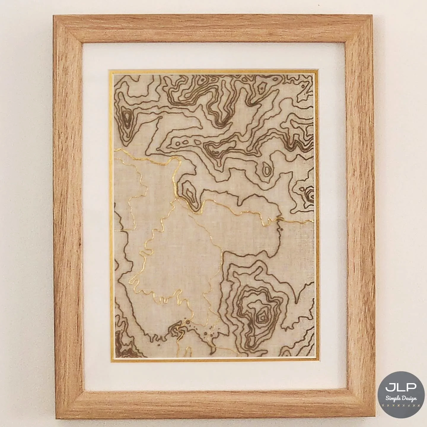 A framed topographic map with engraved contour lines, showcasing elevation changes in black and gold, on a neutral background.