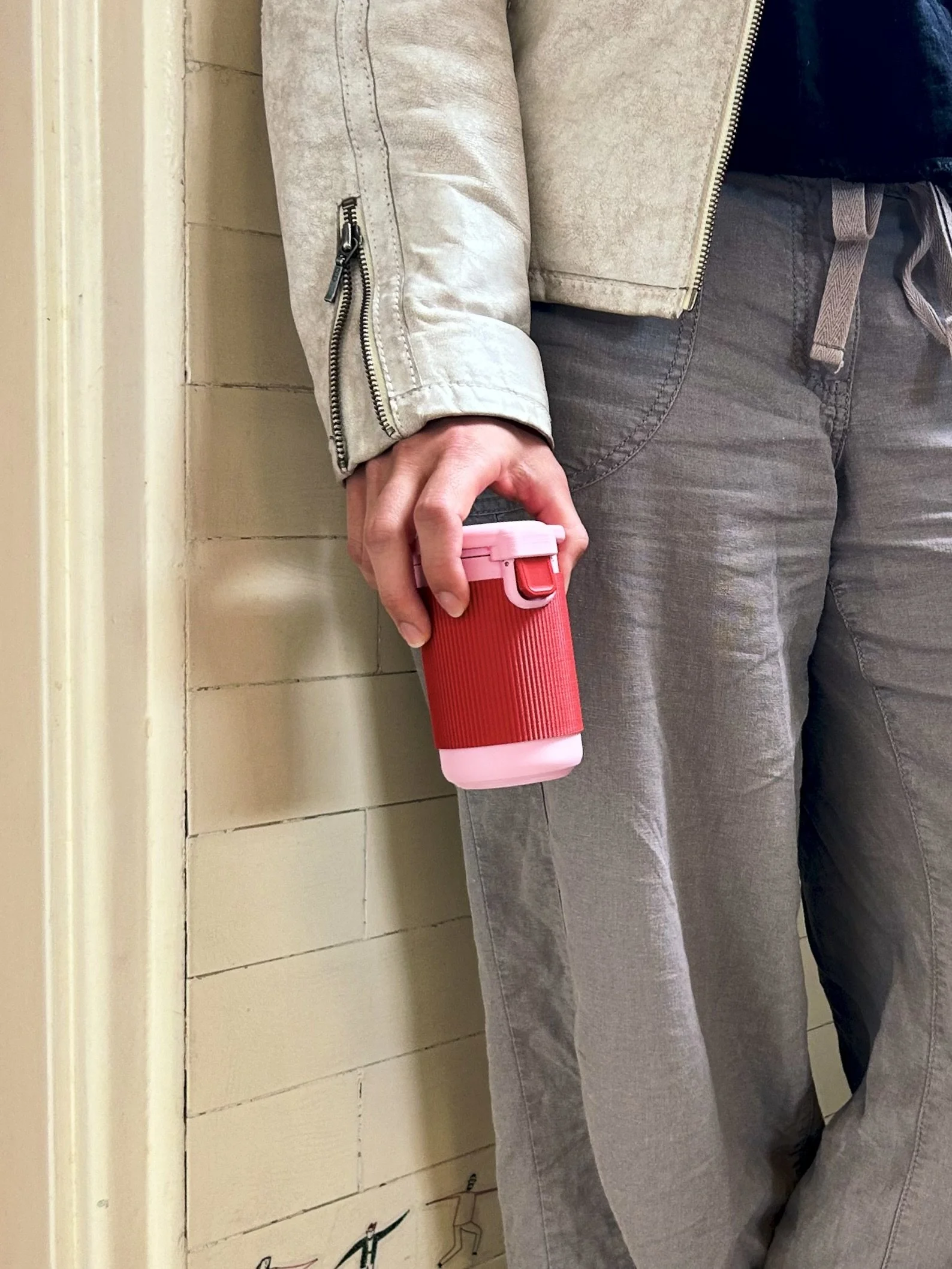 Person standing against a tiled wall while holding Halo menstrual cup rinsing pod in the Very Berry colourway at their side