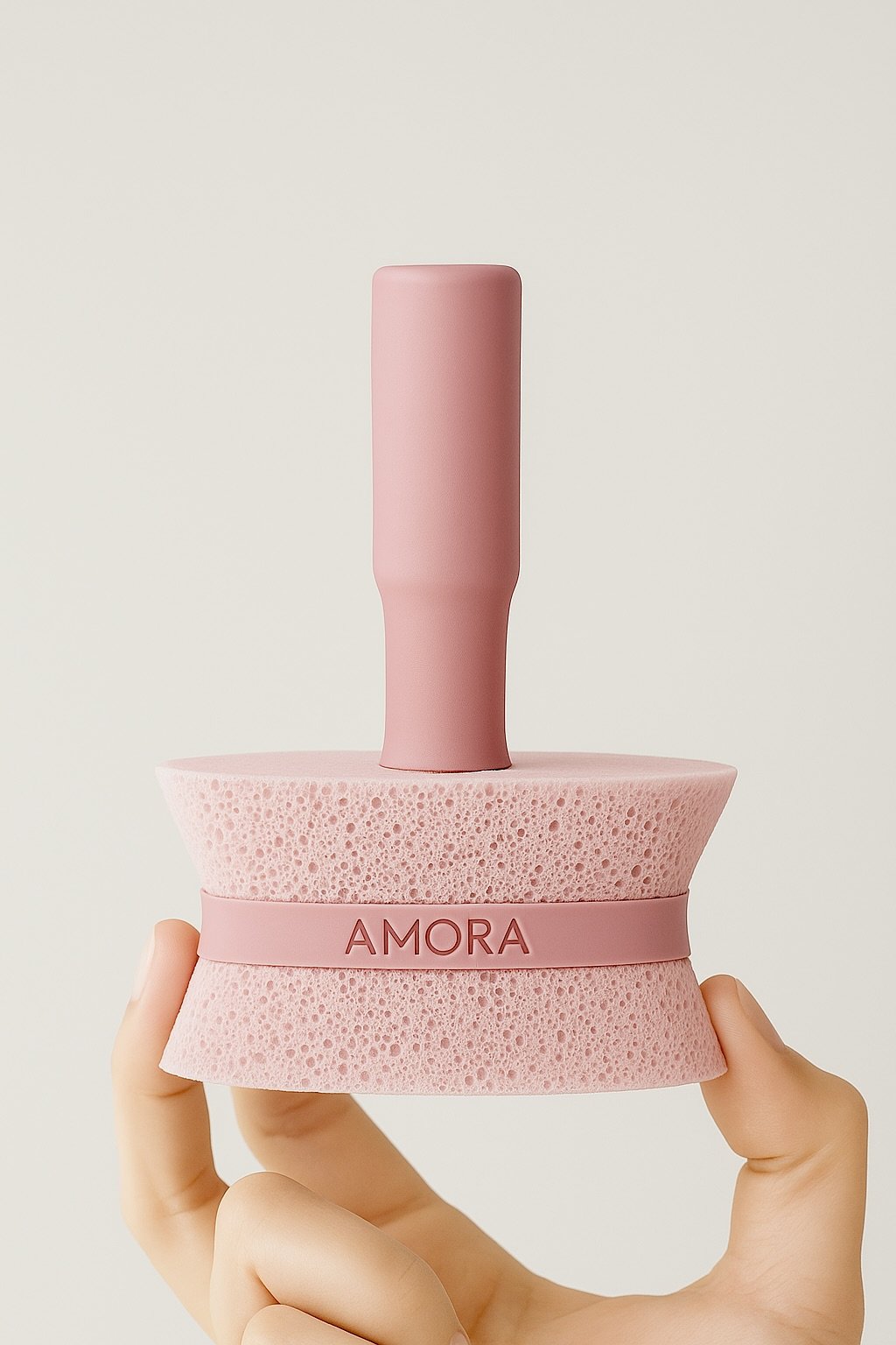 Hand holding Amora cleaning sponge with reusable handle on a neutral background