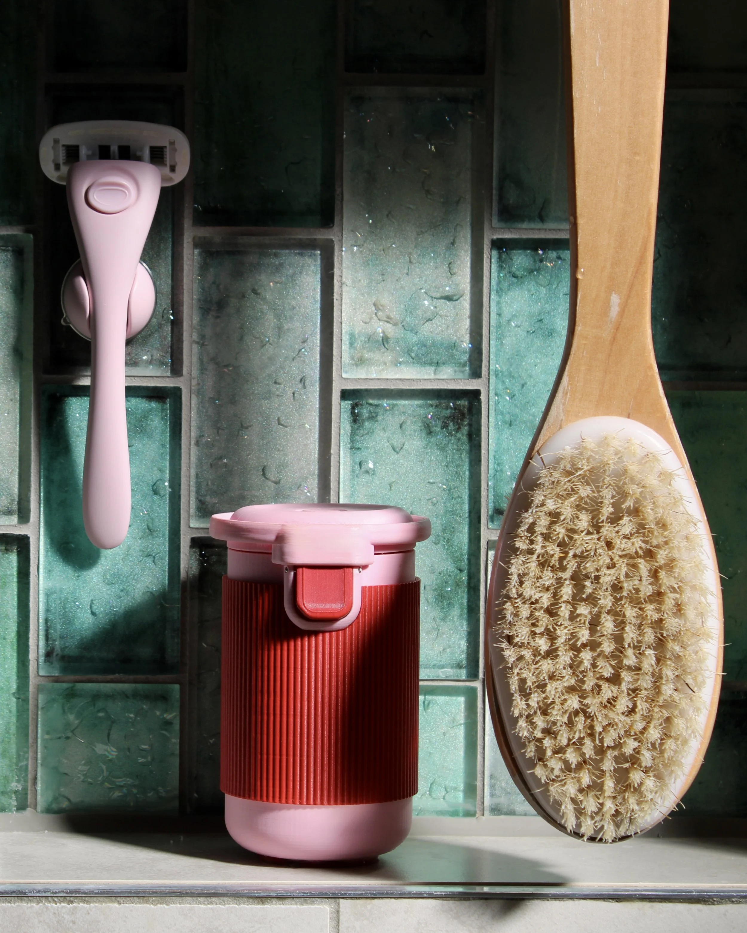Halo menstrual cup rinsing pod in the Very Berry colourway styled on a bathroom shelf against glossy green tiles, shown beside a pink Estrid razor and a natural wooden body brush