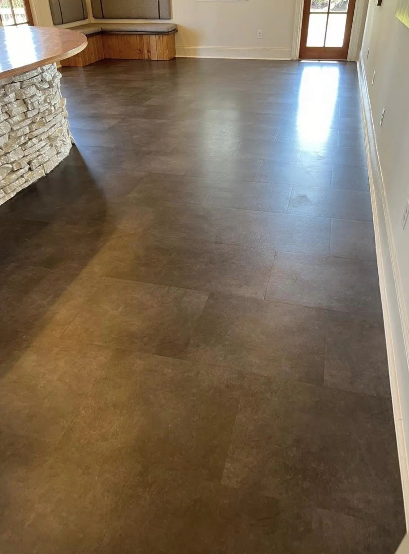 Room with dark brown tiled flooring, a stone accent wall on the left, beige walls, white baseboards, a door with glass panes leading outside, and a built-in seating area with wood paneling in the corner.